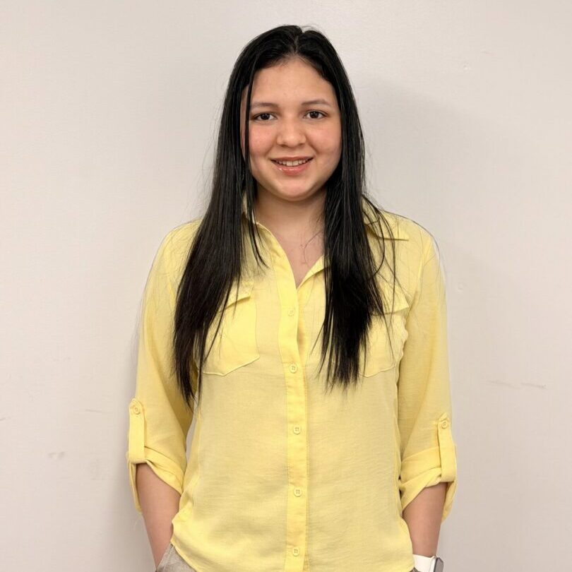 Smiling person wearing yellow blouse, hands in pockets